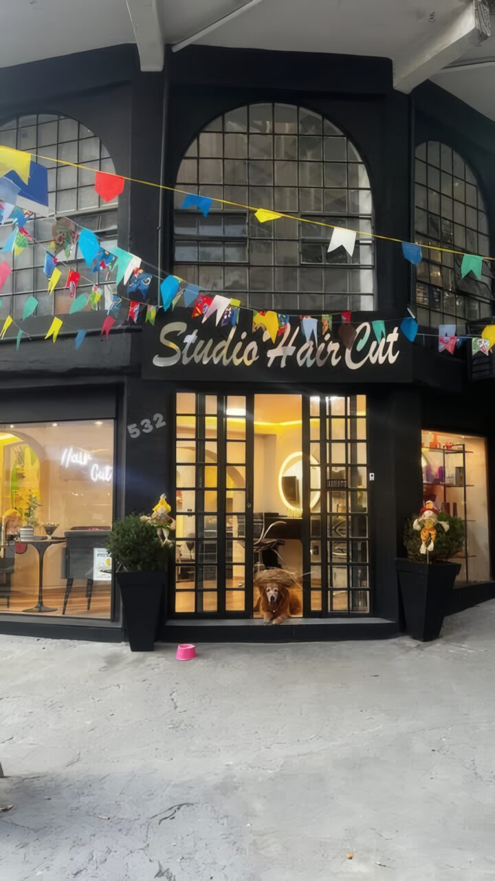 Fachada do Studio Hair Cut de dia, enfeitada com bandeirinhas e com um cachorro deitado na entrada