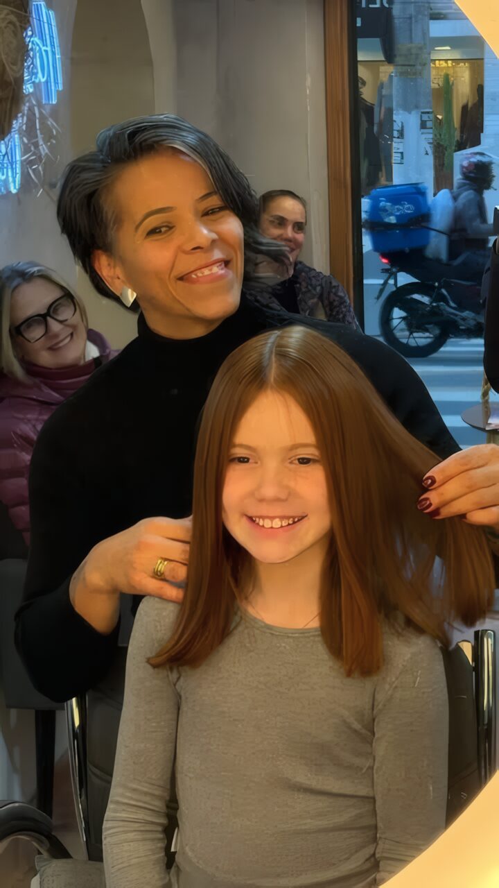 Profissional do Studio Hair Cut sorrindo atrás de uma menina com o cabelo recém-cortado